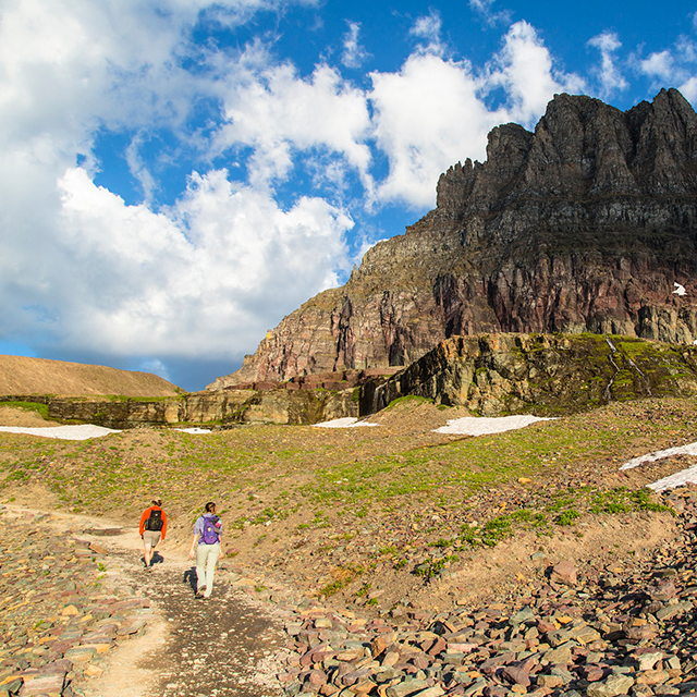 A group of hikers walk on a trail toward a towering mountain in the distance
