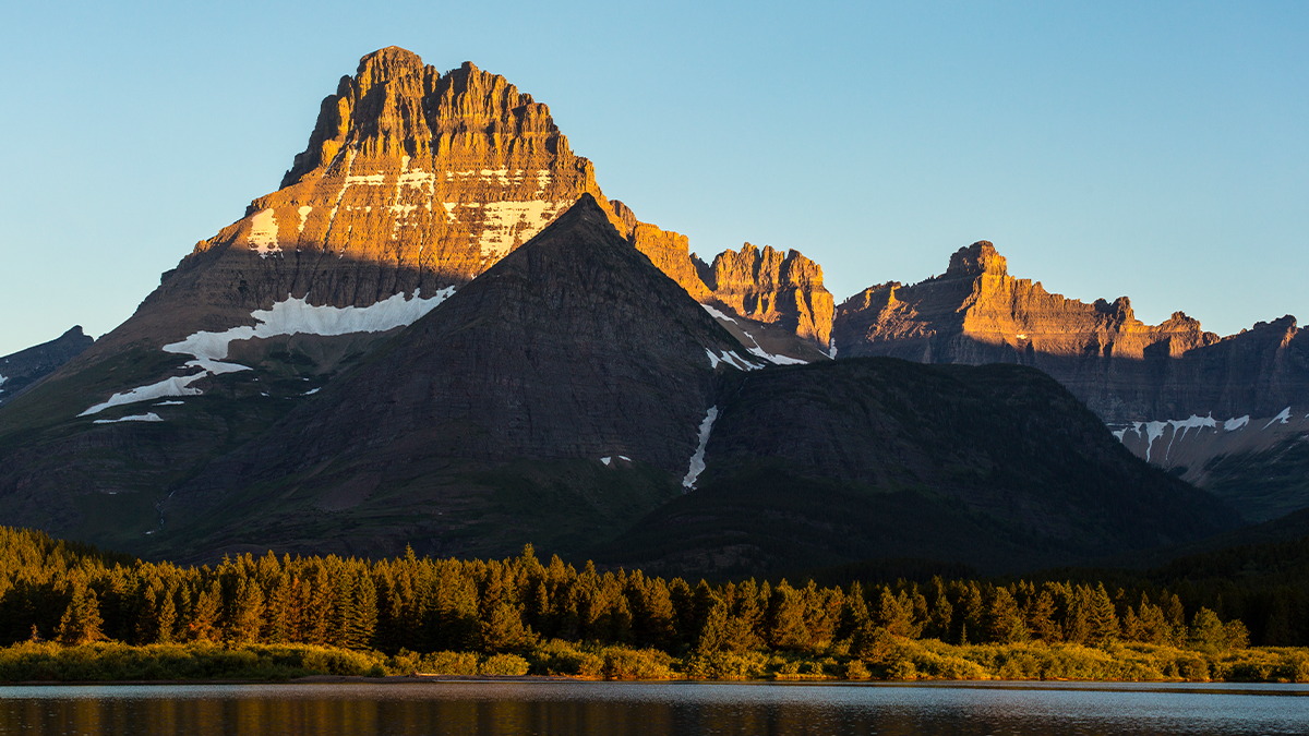 A snowcapped mountain range towers over an alpine lake